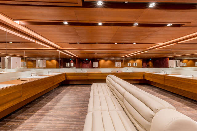 Bathroom sink area with wooden bathroom cabinets and mirrors on three sides and. a white leather sofa in the middle.