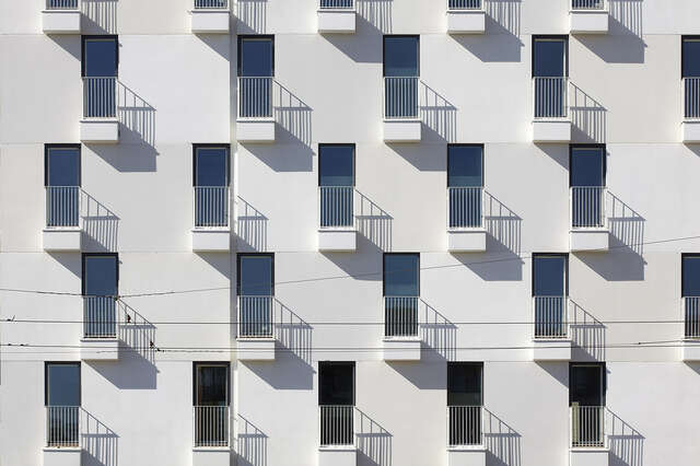 Offset rows of small balconies on a white plastered background.
