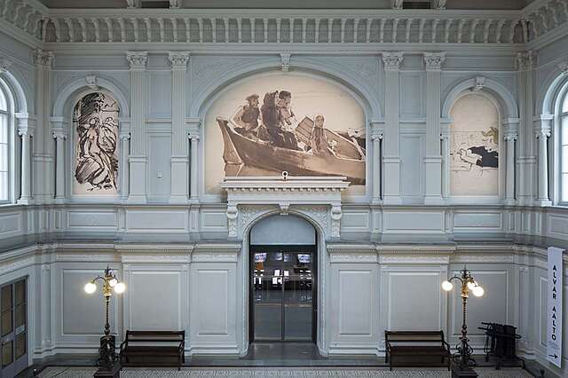 Three murals ton an ornate wall in the museum. A sketch of a woman, a painting of a family on a boat, and a sketch of a child.