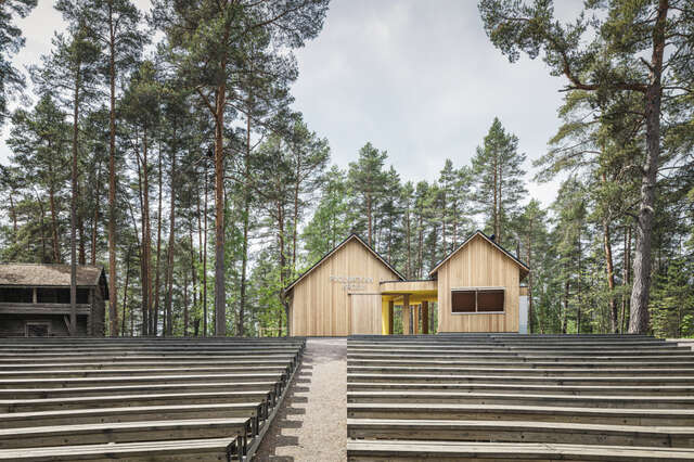 View from the stage up along the stands, two small timber volumes with pitched roofs on top of the hill