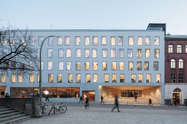 White university building wit offset rectangular windows and a wood covered entrance.