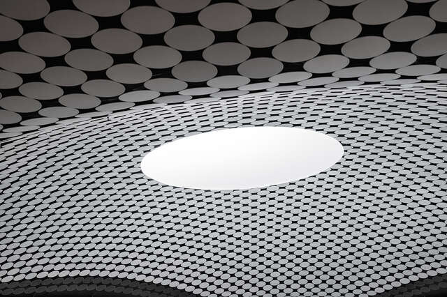 Domed ceiling covered by round white plates and with a circular skylight in the centre.