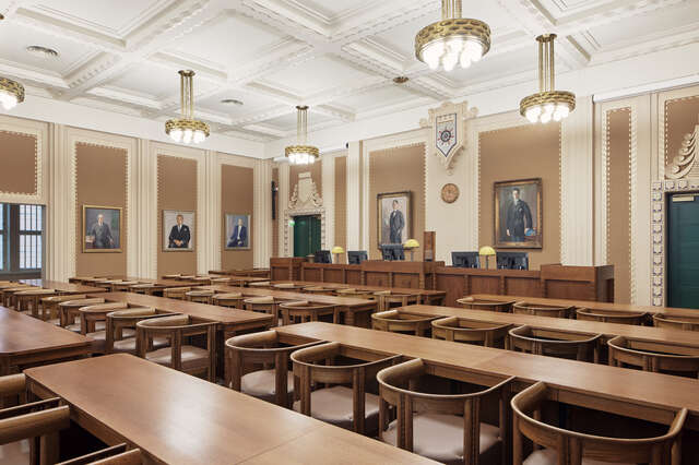 A large room with rows of wooden tables and chairs with portraits hung on the walls.