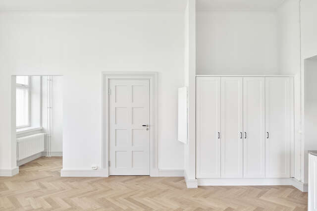 An empty apartment with a wood floor, white walls and cabinets.
