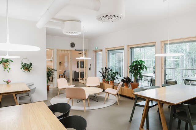 A bright common space with large windows, light wooden furniture, house plants and a lot of natural light.