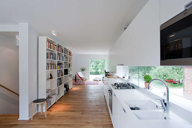 Minimalsitic kitchen with along window as the backsplash and a bookshelf at the opposing side of the space.