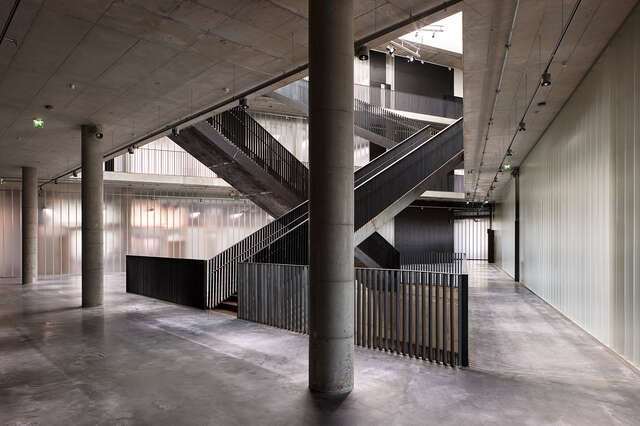 Interior of concrete structure. Long, narrow black staircases in the middle. concrete pillars in foreground.