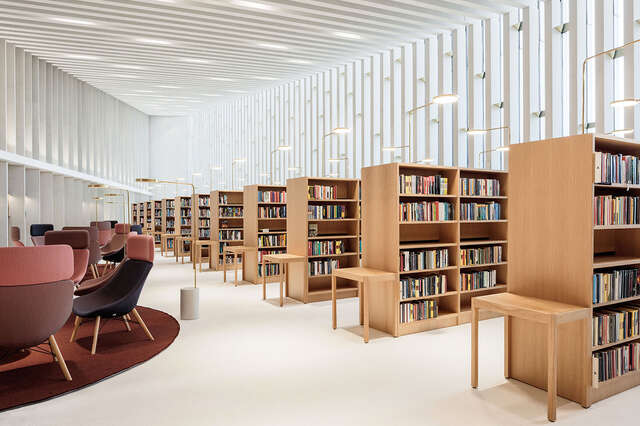 White space with vertical battens in the window wall and joists, wooden bookshelves, burgundy-coloured armchairs