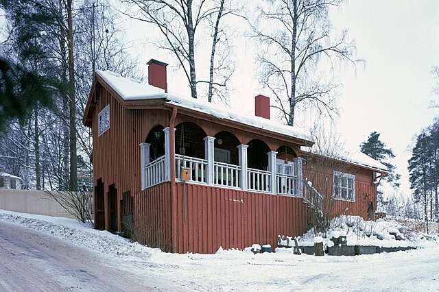 Red timber house with white porch details on a snowy day.