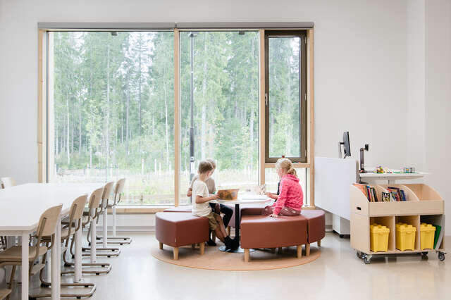 Three children sitting in a classroom around a table.
