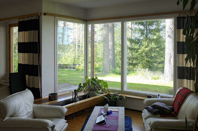 A photo of a house showing the living room with and elegant corner window with a view to the green yard with trees.