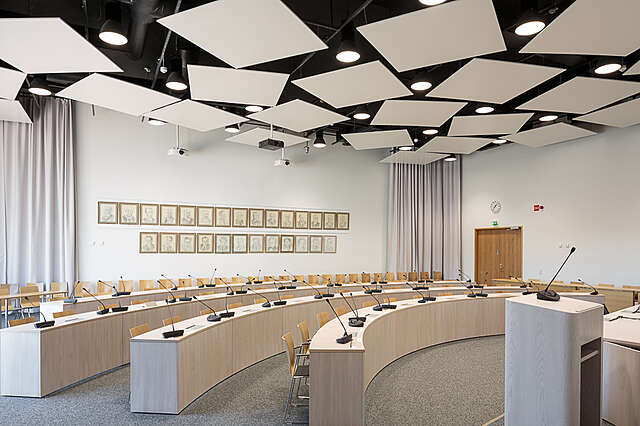 White room with rounded semicircular birch tables for the speakers and white share detailing on the dark industrial ceiling.