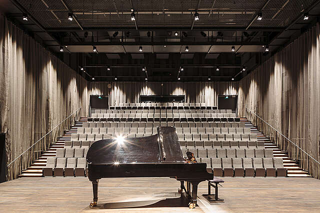 A grand piano on front of seating tows on the back of the hall.