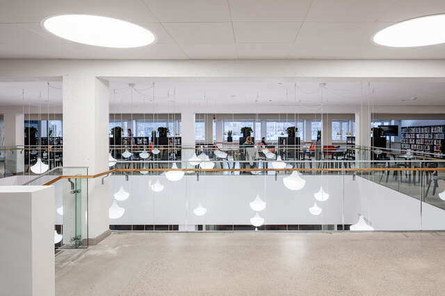 Light fixtures hanging down to the lower floor on the other side of a glass railing.