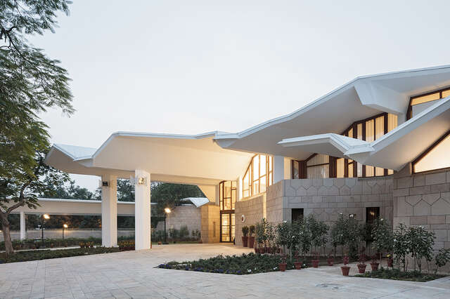 Entrance to the embassy through glass doors, the entrance is covered by the extending white roof that has a complex shape.