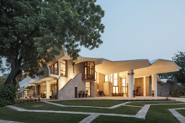 Facade of the building with the lights on, consisting of stone, wood and glass elements.