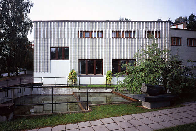 Grey and white facade with baton shaped glazed tiles and brown framed windows.