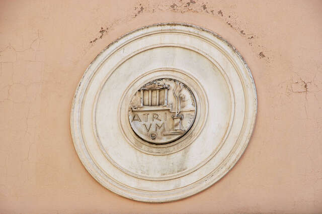 White circular sculpture with a temple and a sculpture depicted in its middle with the word Atrium.