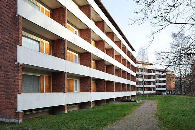 Facade of a red-brick apartment building with white balconies and wooden doors.