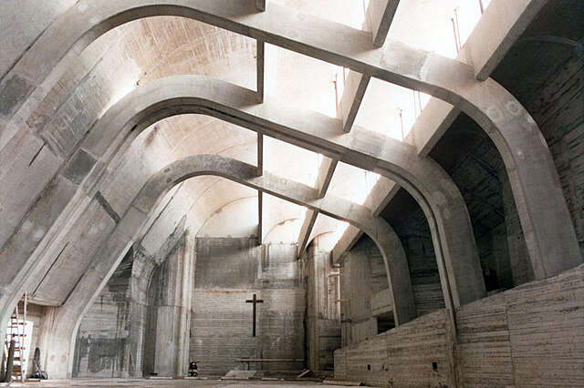 Concrete interior during construction with only a cross above where the altar would be.