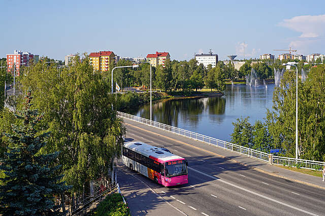 Red bus on a bridge over water, in the distance some blocks of flats