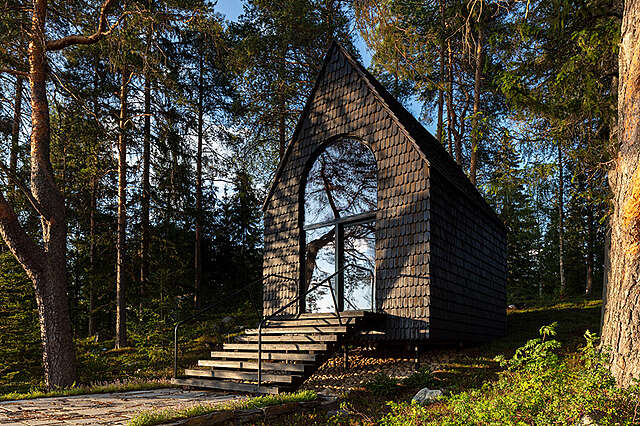 Dark-covered small building with a steep roof and glass door