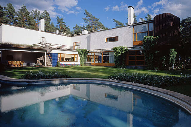 Back garden of a white two storey house with wooden window frames with a pool