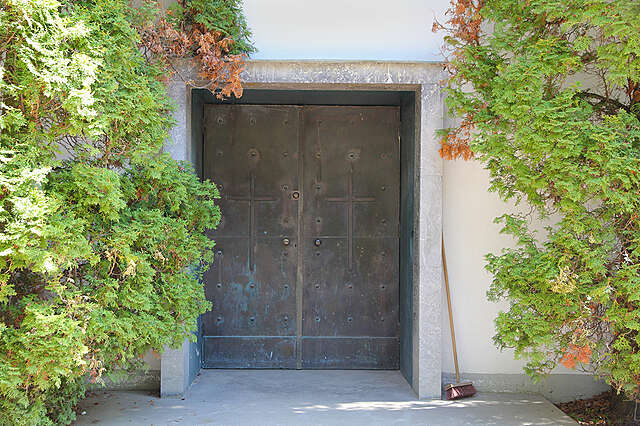 Metal entrance doors to a white chapel with trees on both sides.