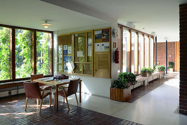 Interior with large windows, brick details, a bulletin board and a small table with chairs.