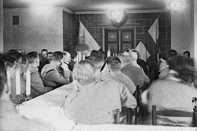 men sitting at a long table and others around it.