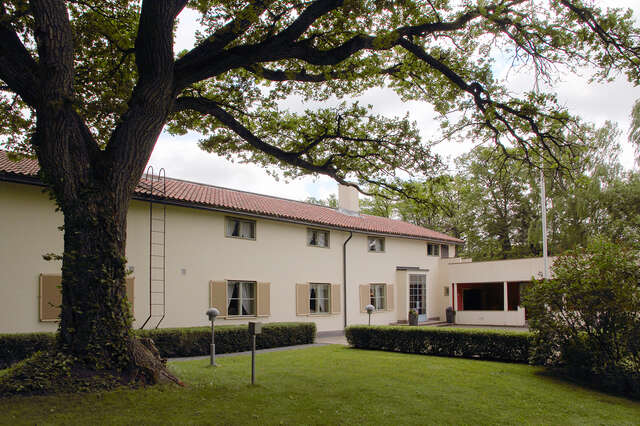 Long cream colored building with window panes and a yard.