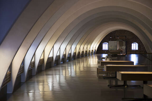 Room with curved roof supported by white beams that are illuminated indifferent white and blue shades.