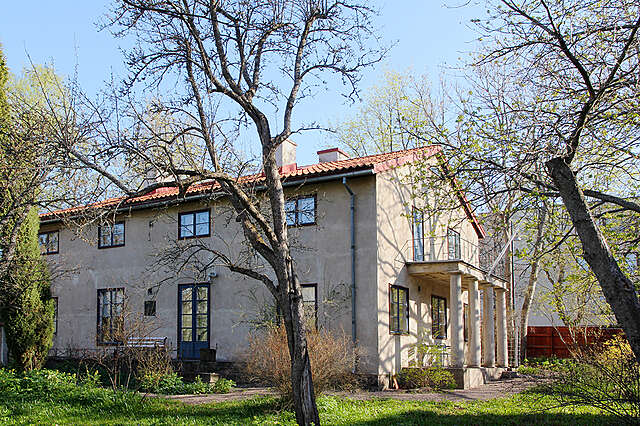 House with a pitched roof, grayish white render, blue framed windows and doors.