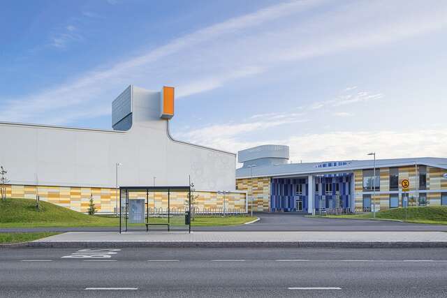 Buildings with differently colored panels on the walls and grey ceilings, a bus stop at the front.