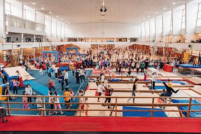 Sports hall with gymnastics equipment in the front and soccer in the back, children are playing freely.
