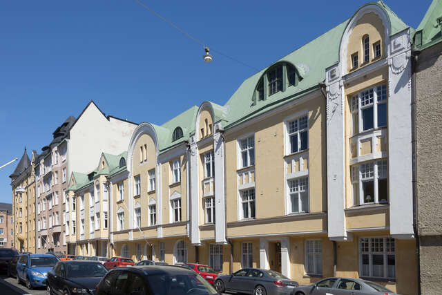 Yellow house with white grid windows and ornaments and a green roof.