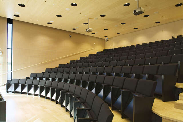 Auditorium with wooden surfaces and black seats.