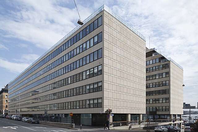 Long office building made out of beige stones.