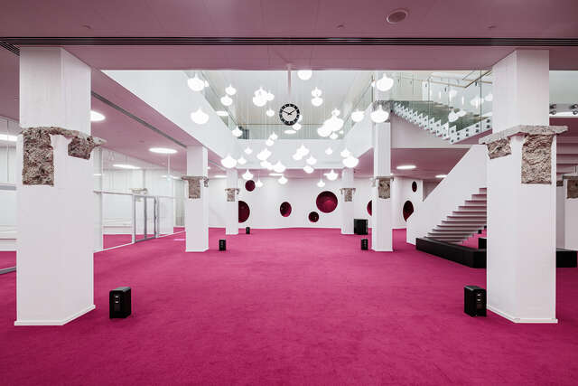 Space with bright pink carpet and several light fixtures as well as white columns.