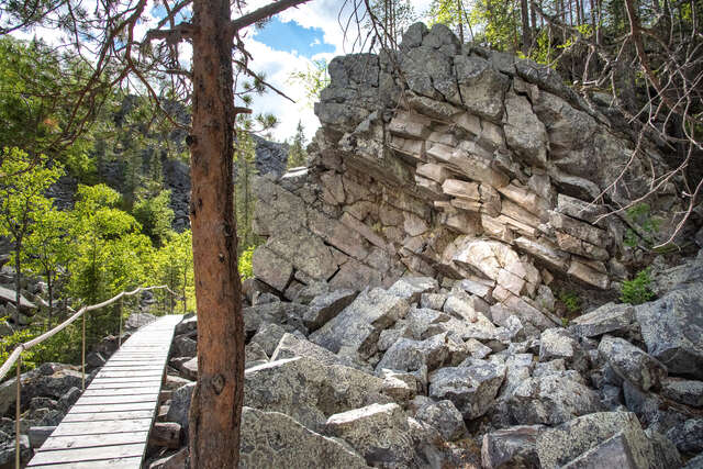 Large rocky formation with a tree and wooden pathway next to it.