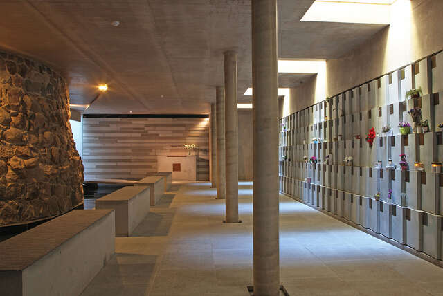 Interior with stone elements and plants and candles on the right wall.