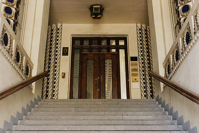 Entrance stairs with wooden railings and very ornate walls with blue and gold details.