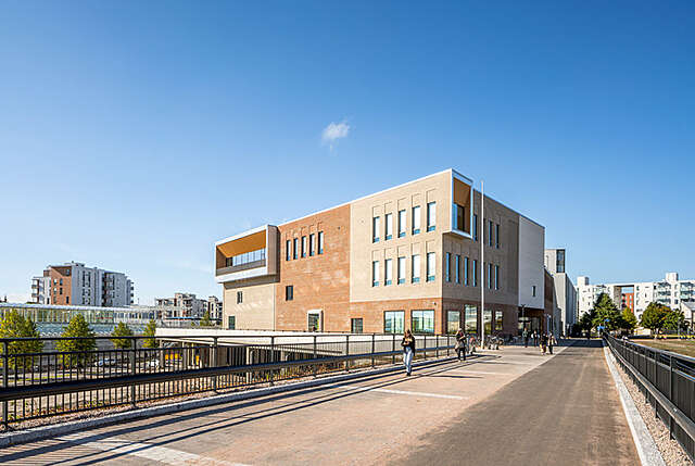 Brick facade of a school building with several distinct small windows and larger square windows
