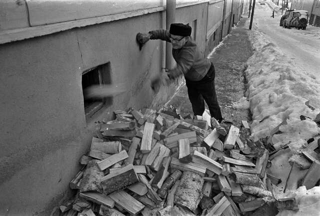 Old man throws logs into a hole in the wall.