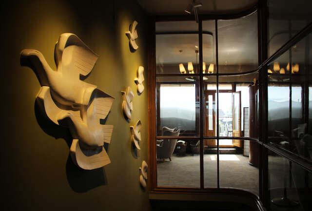 Bird sculptures on the wall, a sitting area and the balcony are visible through the glass wall.