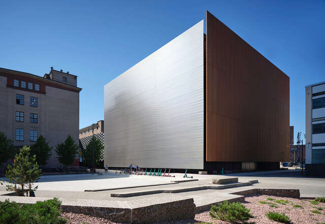 Large cube shaped building with large metal wall. Blu. sky in background,