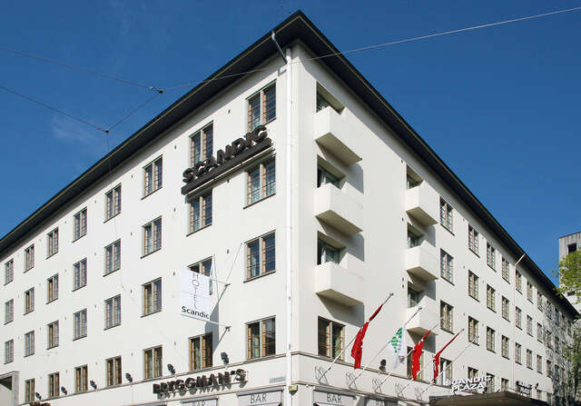 White hotel building with grid windows and shops on the first floor.