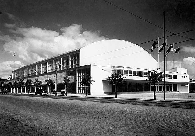 White building with an arched ceiling and large grid windows on the upper half of the building.