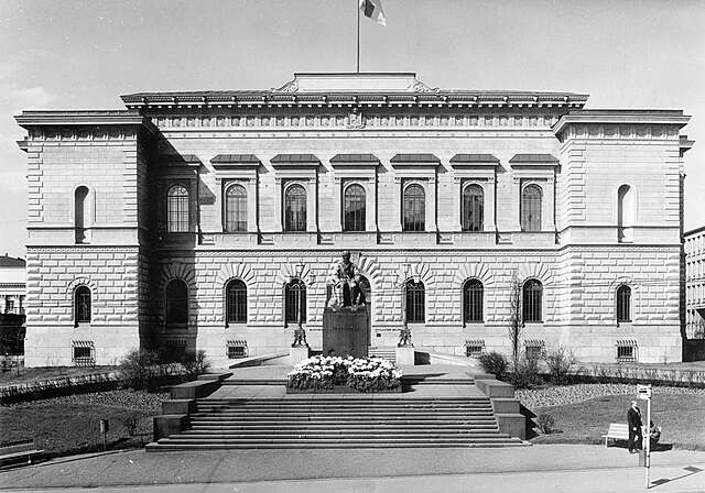 White stone facade with a sculpture in front of it.