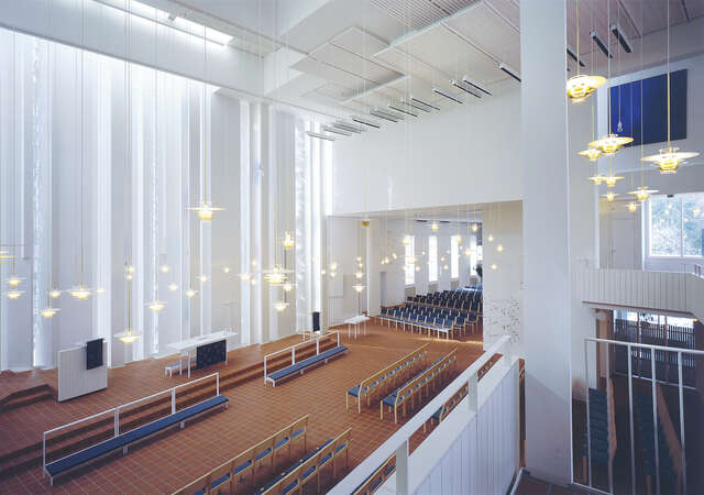 Spacious and white church interior with a view of the altar with tens of lamps hanging at different heights.